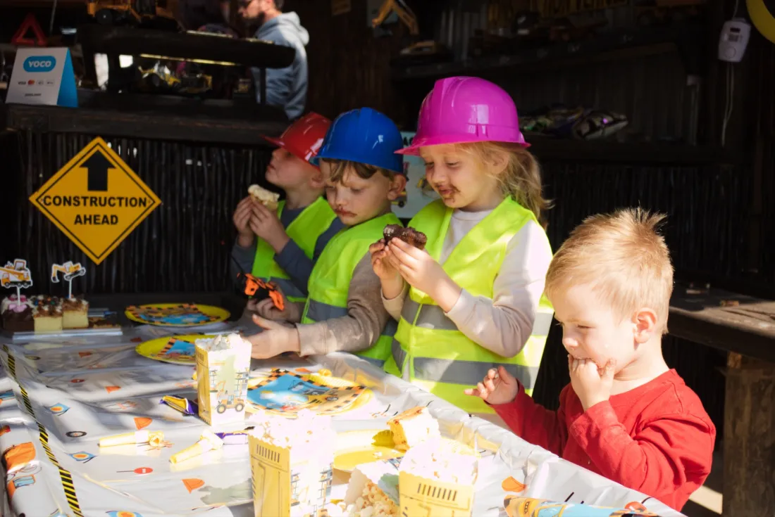 A group of children in hard hats and hi-vis vests playing together at a birthday party