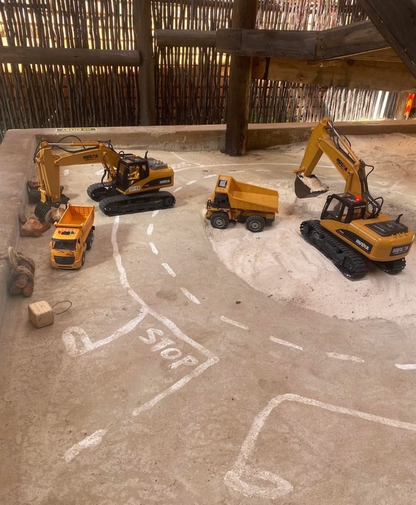 Remote-control excavators and dump trucks parked on the sandy dig course at Backyard Diggers