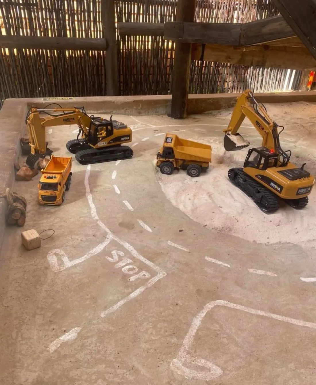Remote-control excavators and dump trucks parked on the sandy dig course at Backyard Diggers