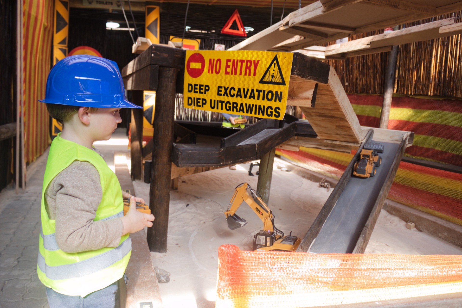 A young operator in a blue hard hat beside the deep excavation sign on the dig course