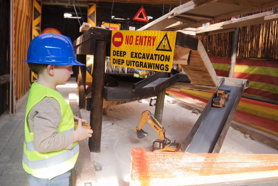 A young operator in a blue hard hat beside the deep excavation sign on the dig course