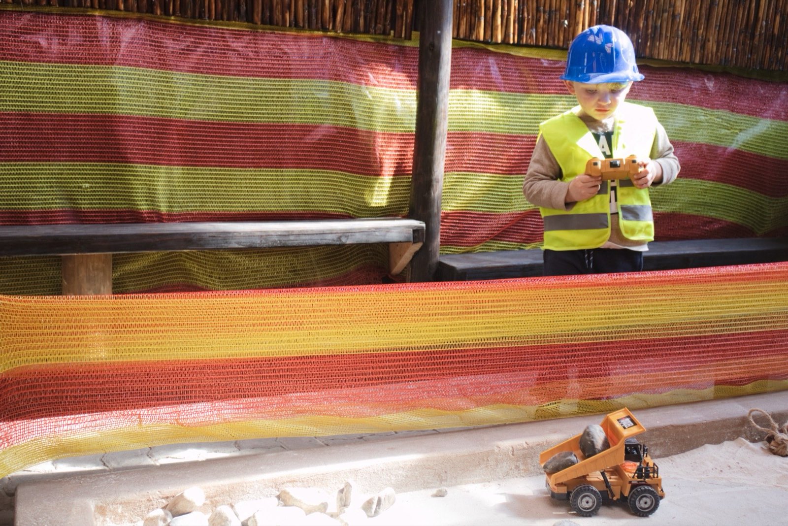 A child steering a remote-control dump truck along the sandy course under the shade netting